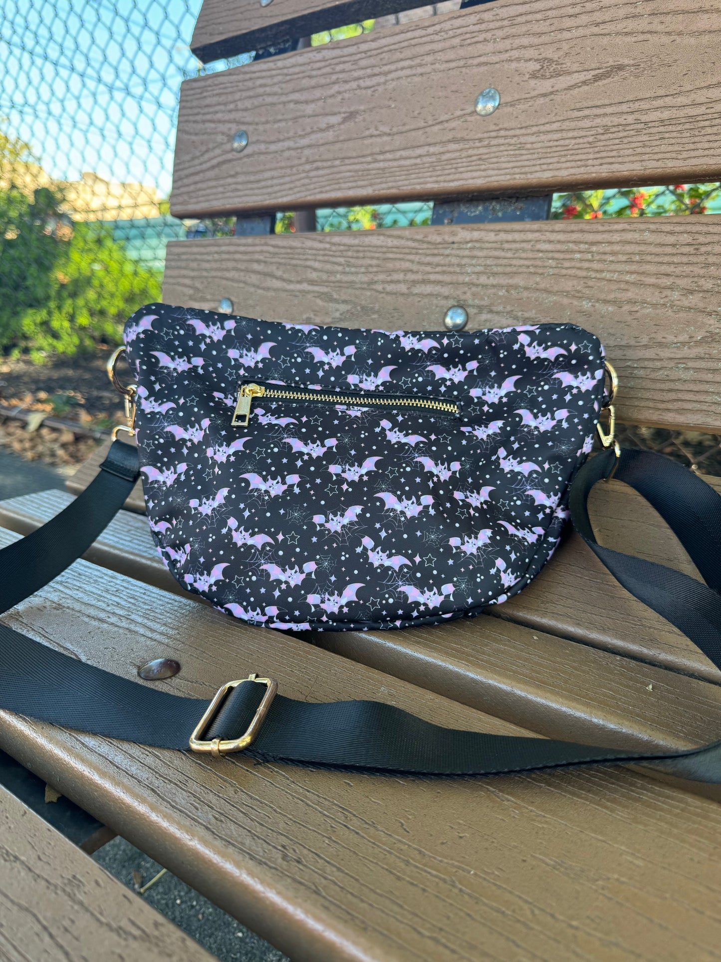 Black crossbody bag with pastel pink and purple bats, spiderwebs, stars and gold zipper hardware