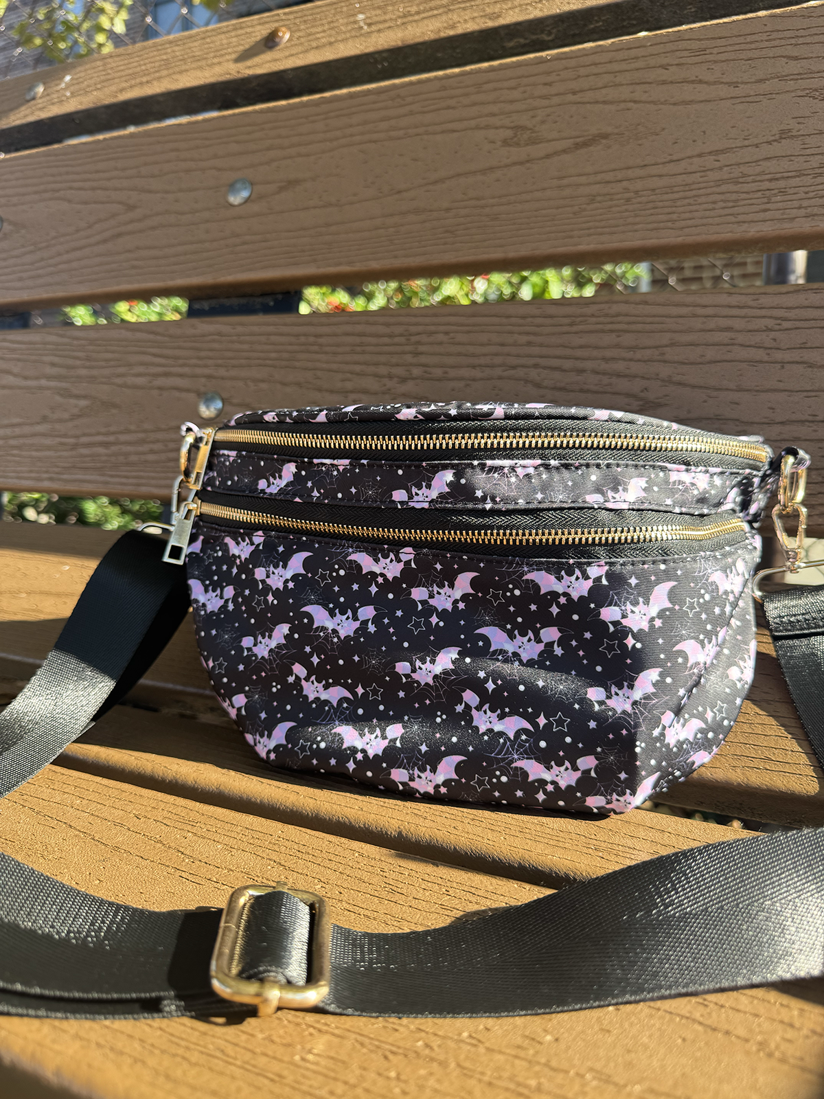 Black crossbody bag with pastel pink and purple bats, spiderwebs, stars and gold zipper hardware
