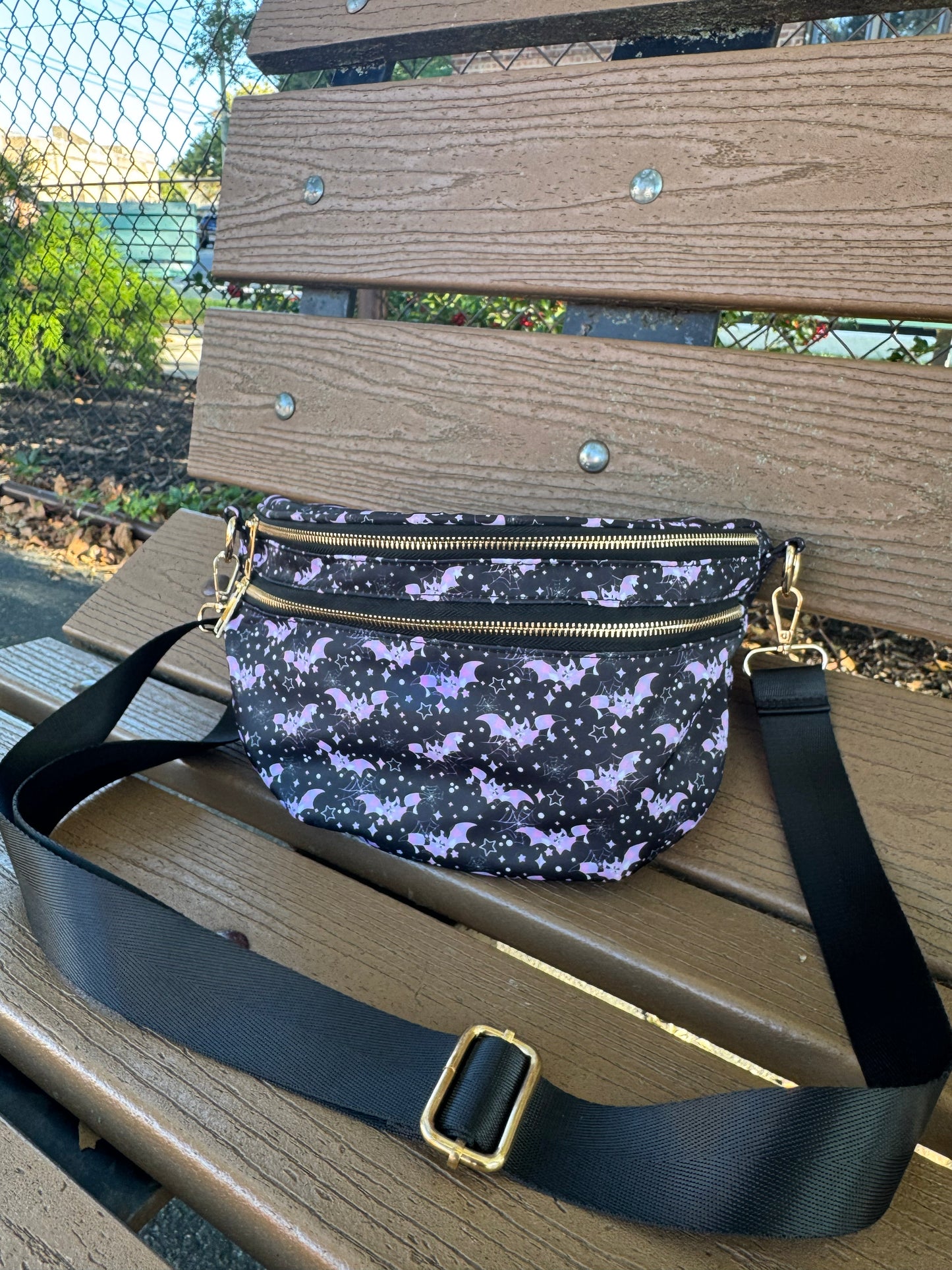 Black crossbody bag with pastel pink and purple bats, spiderwebs, stars and gold zipper hardware